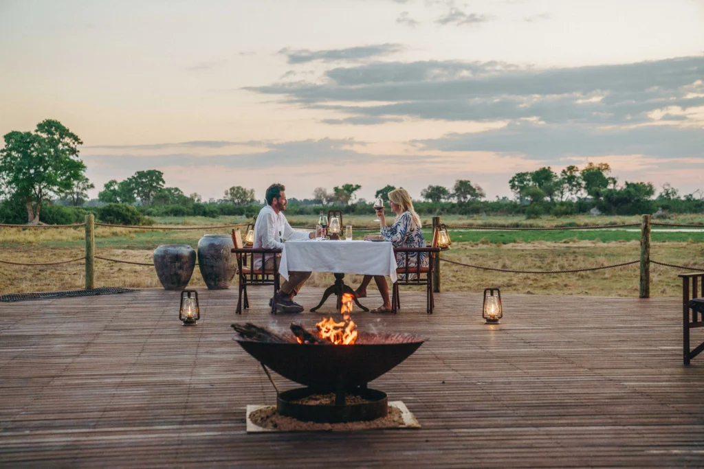 a couple sit at a small table next a fire at Atzaro Okavango