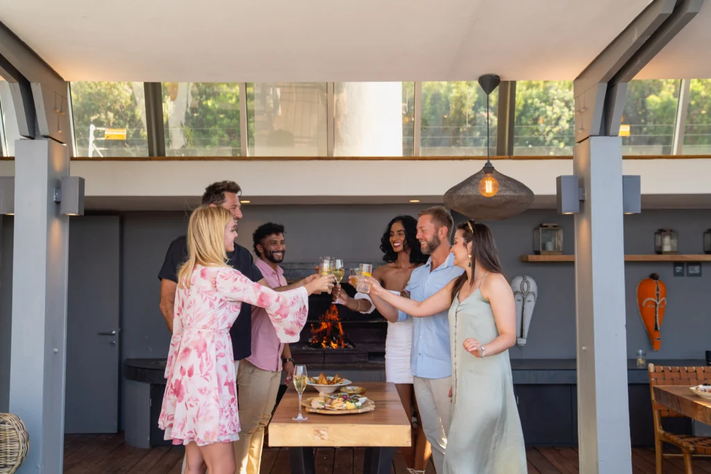 A group of men and women stand around a dining table toasting their wine glasses 