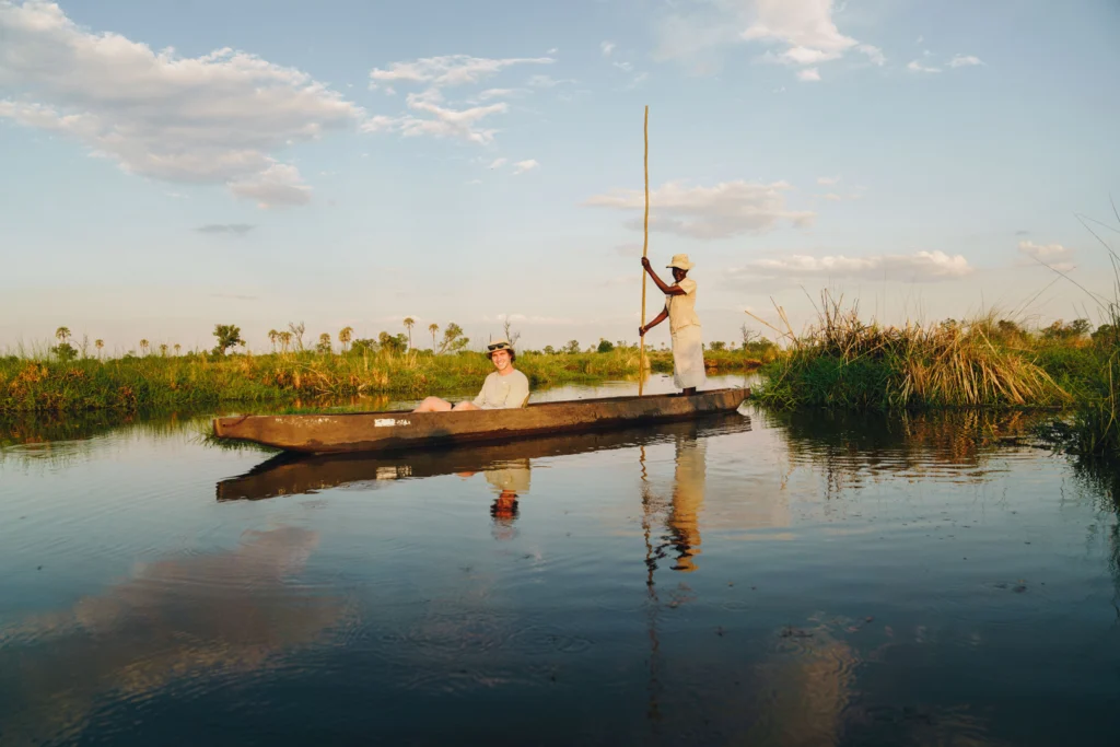 a traditional dug out canoe is polled through water with a person sitting at the front.