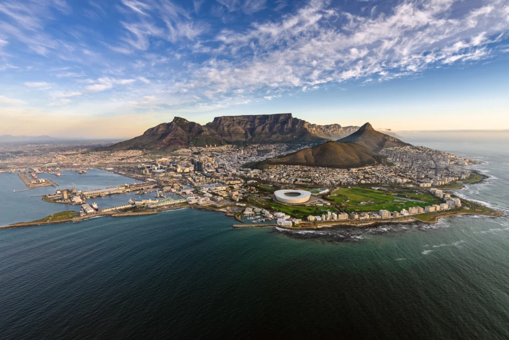 Aerial view of Cape Town with Table Mountain, the city skyline, and the surrounding coastline stretching into the horizon.