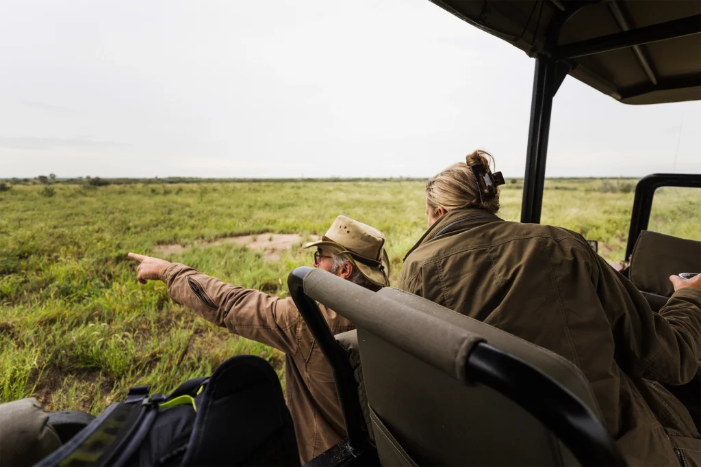 Two people in a safari vehicle observing the vast plains during a game drive in southern Africa.