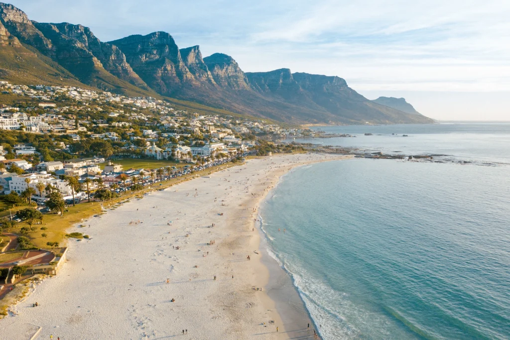 Camps Bay beach with turquoise waters, white sand, and the Twelve Apostles mountain range in the background.