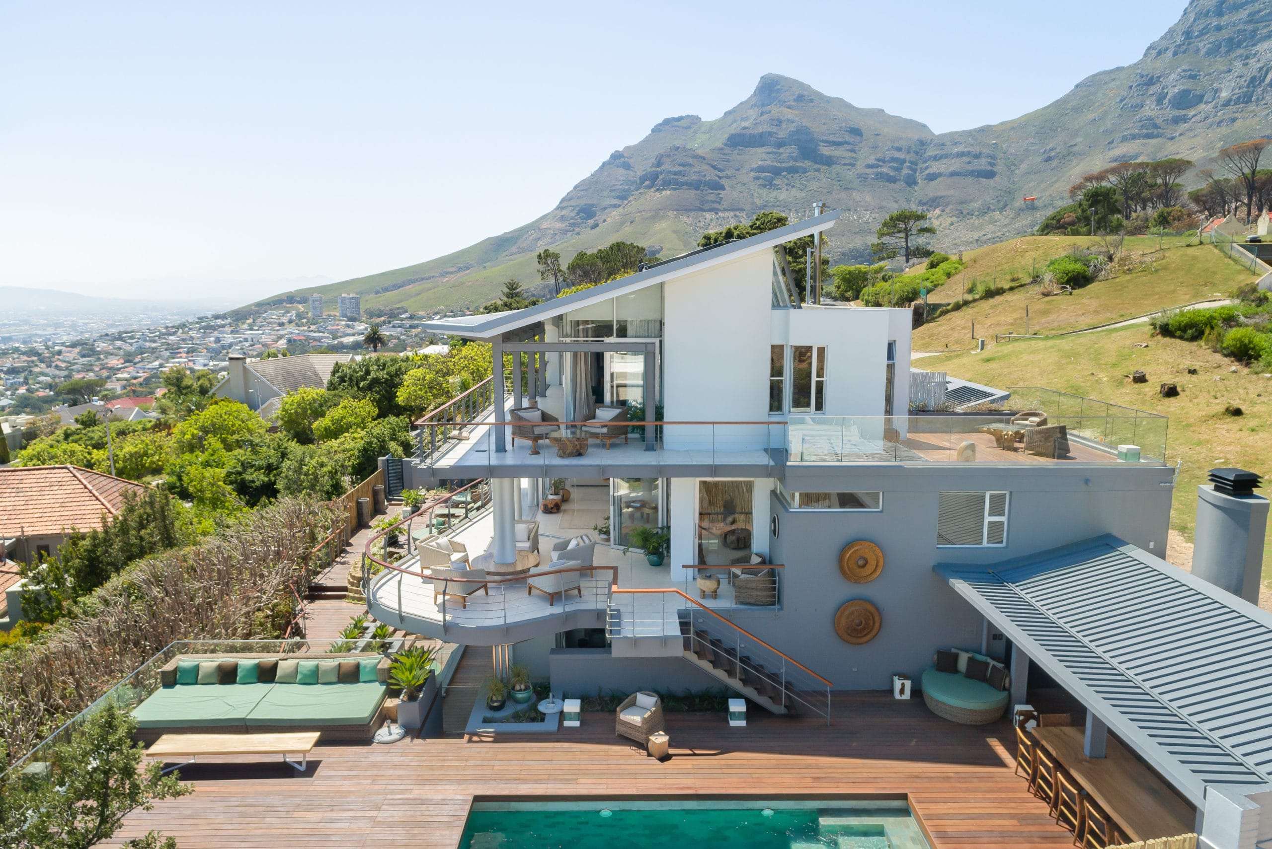 Aerial view of the modern Atzaró Cape Town luxury Small hotel featuring a multi-level deck, swimming pool, and outdoor lounge areas with Table Mountain in the background.