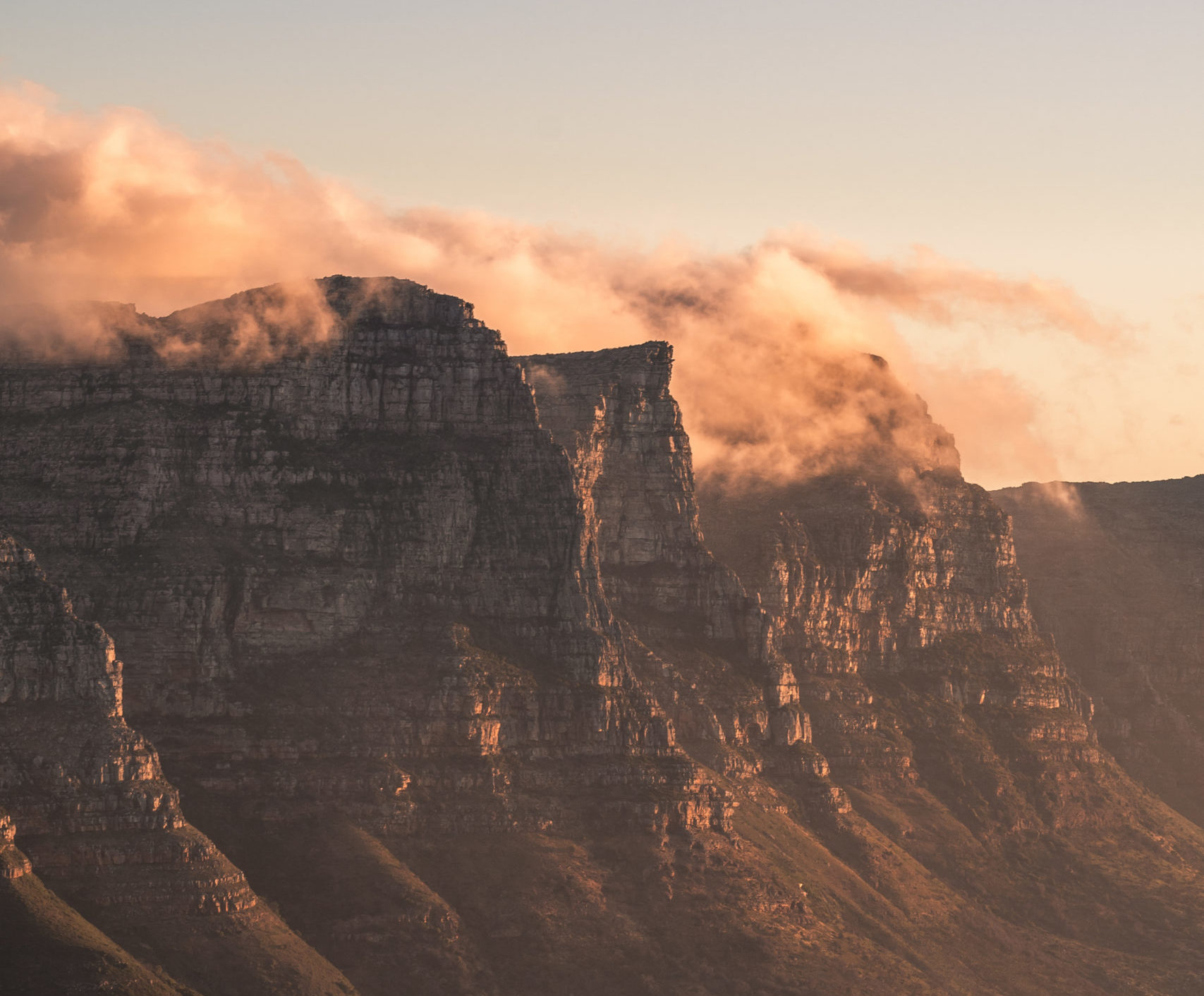 Sunset view of the Twelve Apostles mountain peaks shrouded in golden clouds above Cape Town houses.