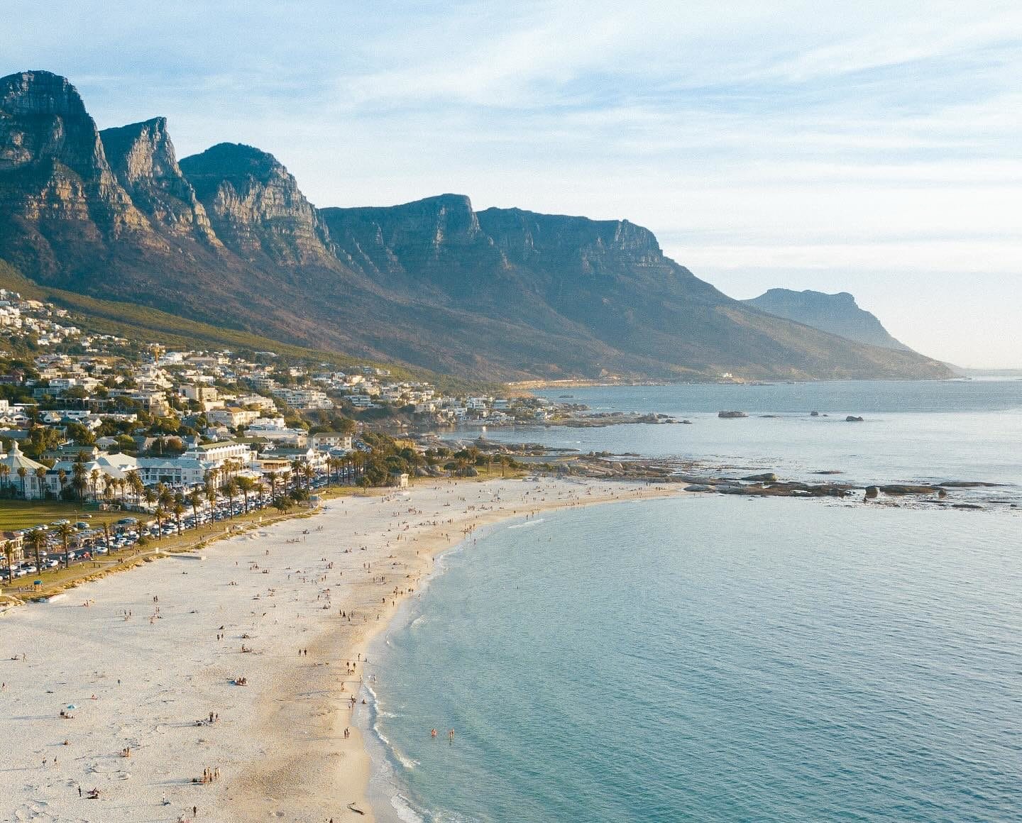 Aerial view of the white sands of Camps Bay beach and the turquoise Atlantic Ocean with the Twelve Apostles mountain range in the background, Cape Town.
