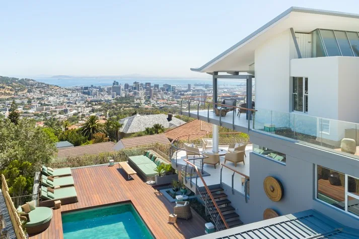 Exterior of Atzaró Cape Town Luxury Hotel featuring a spacious wooden deck, private swimming pool, and sun loungers, offering a panoramic view of Atzaró Cape Town city and sea.