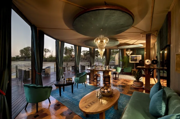 Luxurious interior design of the wine cellar and tasting lounge at Atzaro Okavango Camp, featuring green velvet seating, elegant chandeliers, and open views of the African savanna.